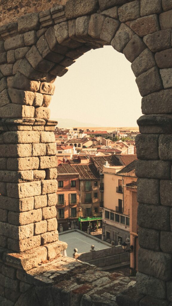 Detail of a single arch of the Segovia Aqueduct with a view looking through it, showcasing the precision stonework and the landscape beyond.