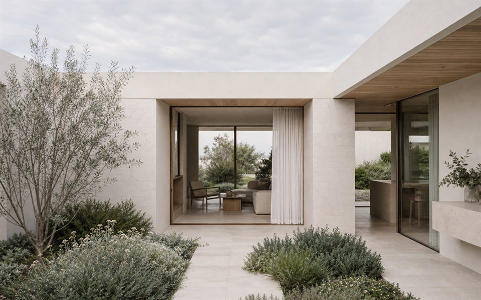 Sheltered contemporary courtyard house with pale stone, timber soffits and coastal planting.