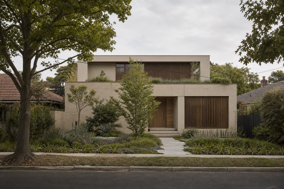 Restrained contemporary house facade with pale brick, timber screens and established street trees.