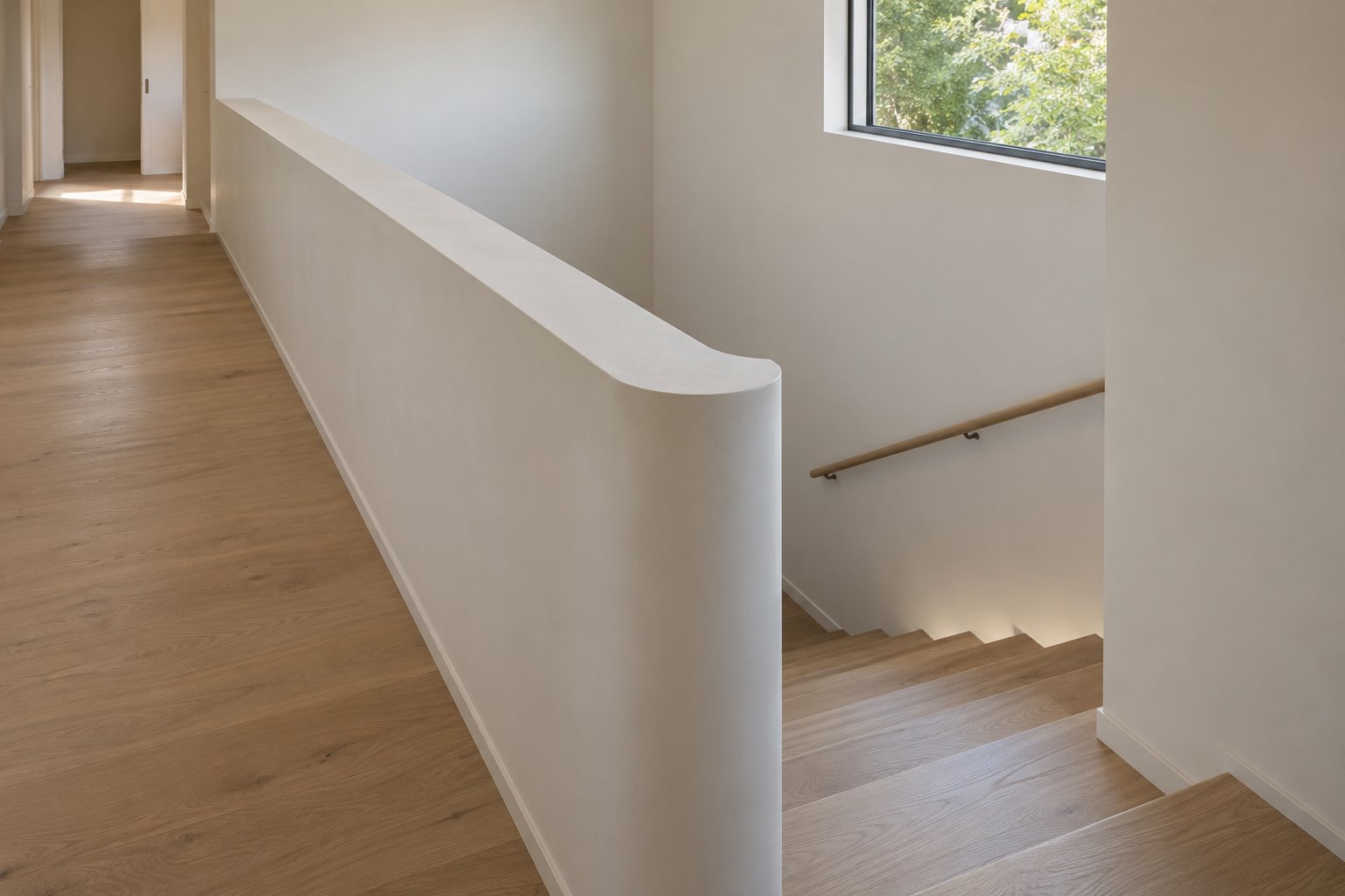 A solid white wall curves around an internal stair opening beside a timber upper landing, with a separate rail along the stair wall.